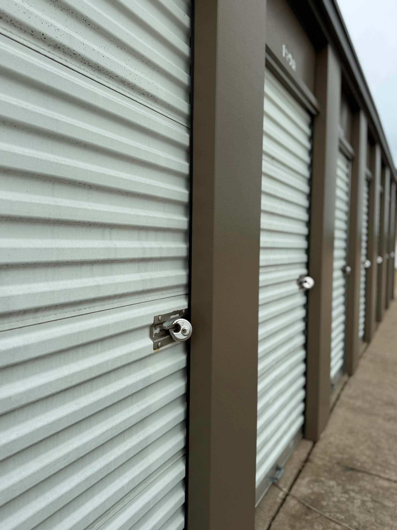 Row of white corrugated metal storage units with brown frames and silver disc locks.