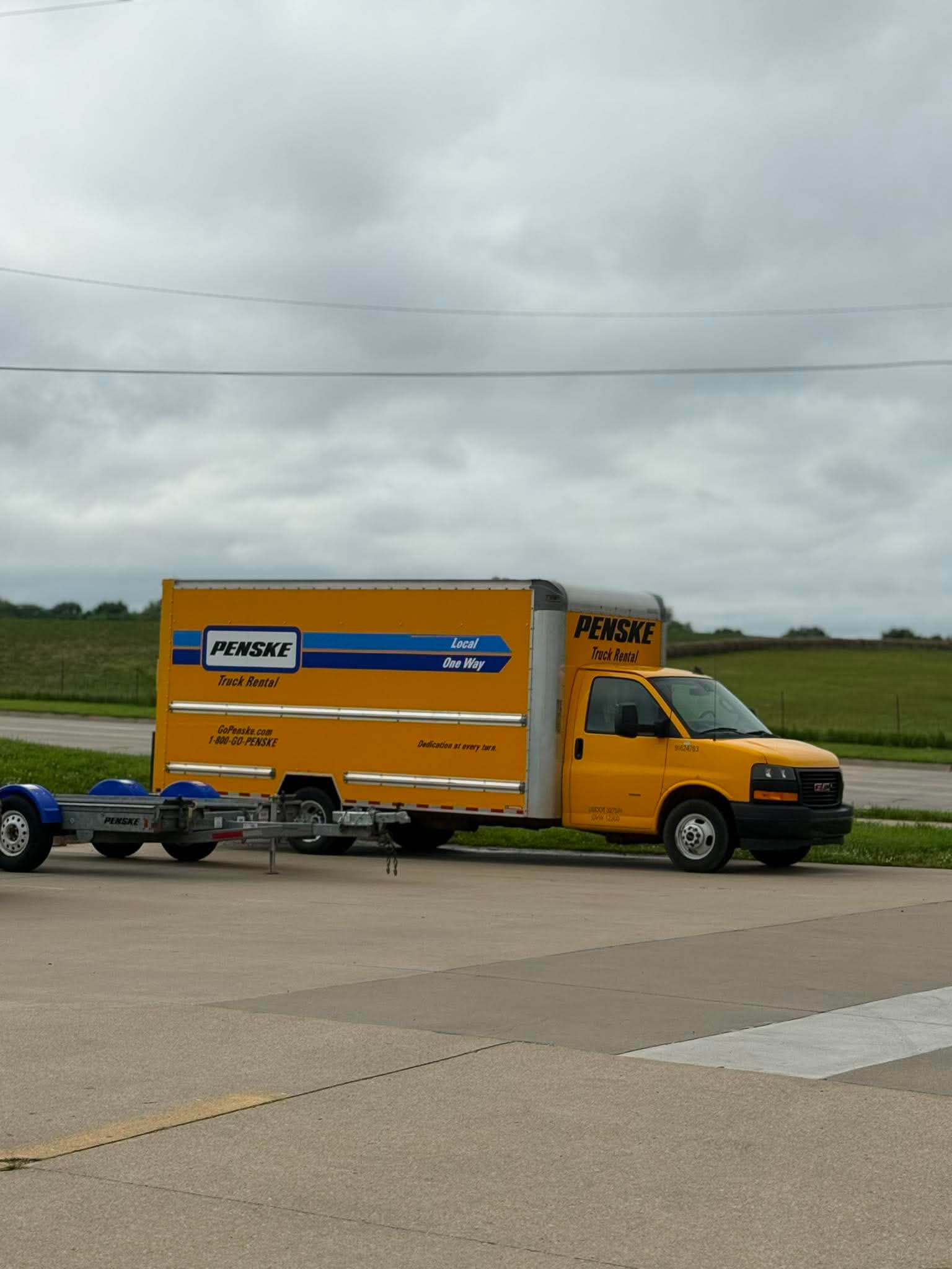 Yellow Penske rental truck with a car carrier trailer parked on a paved lot.